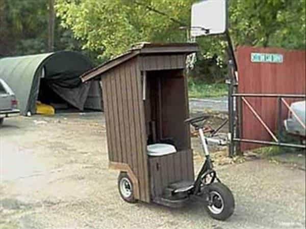 A Weird Wood creation of a tri-wheeled scooter with a small shed and toilet built over the seat area.