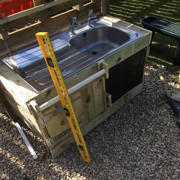 A piece of curtain dowel rod makes a perfect paper towel or yard towel holder on this pallet mud kitchen. Large gate hinges make a sturdy and decorative touch to the door.